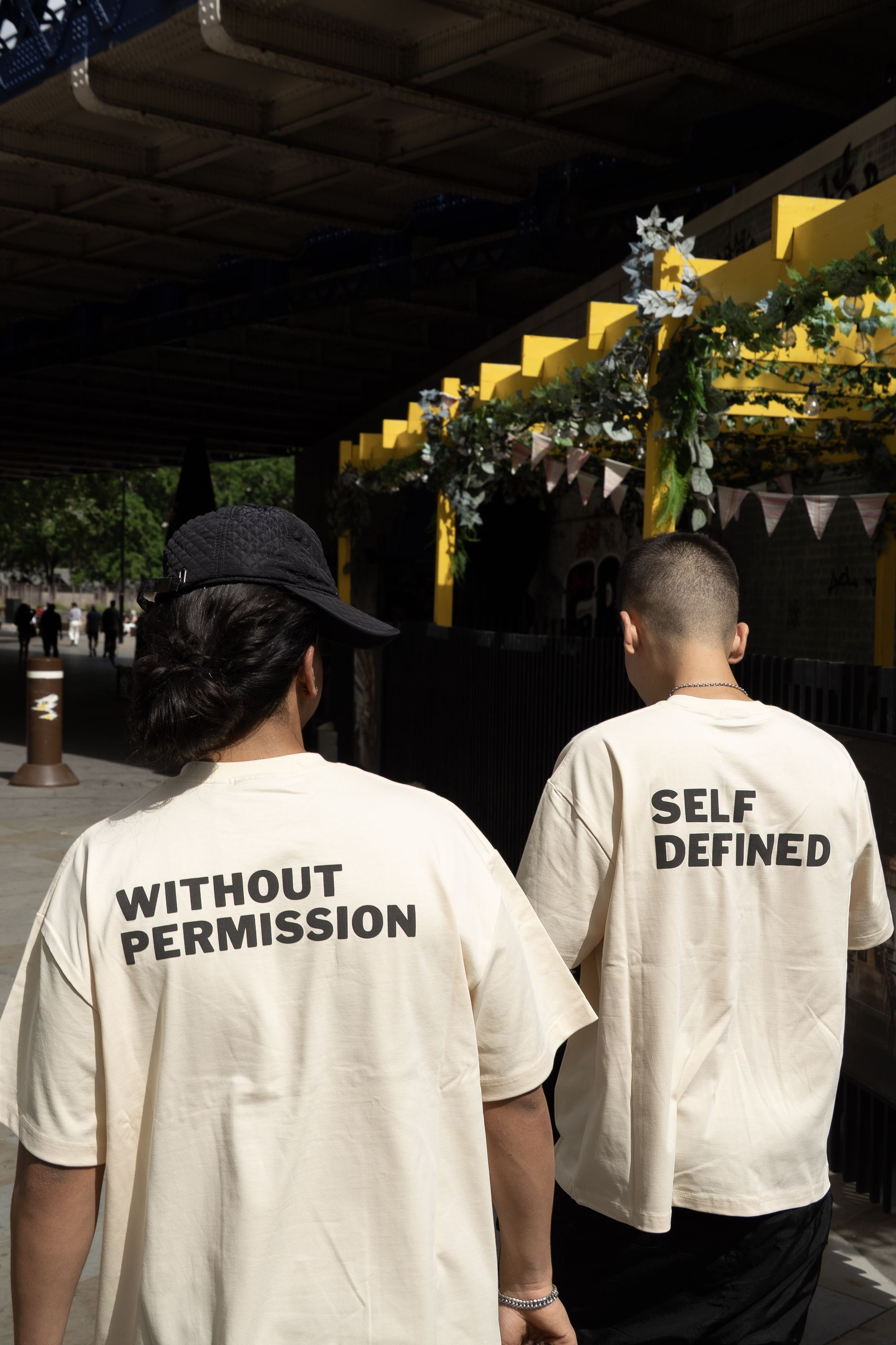 Three models seated on a bench wearing the oversized DROP 001 tee in seedpearl